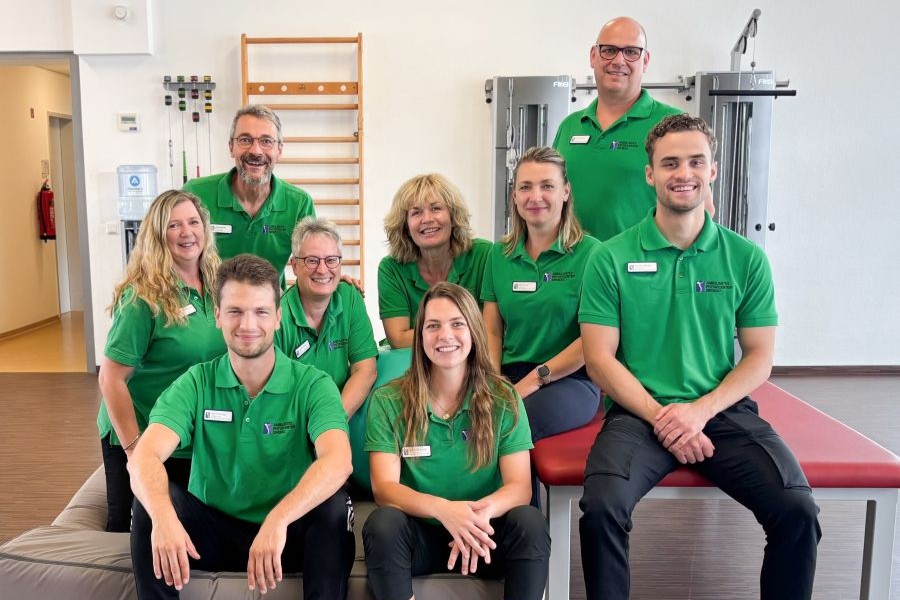 Das neunköpfige Physio-Team unseres Physio-Centers in grünen Shirts im Trainingsraum aufgereiht zum Gruppenbild. 