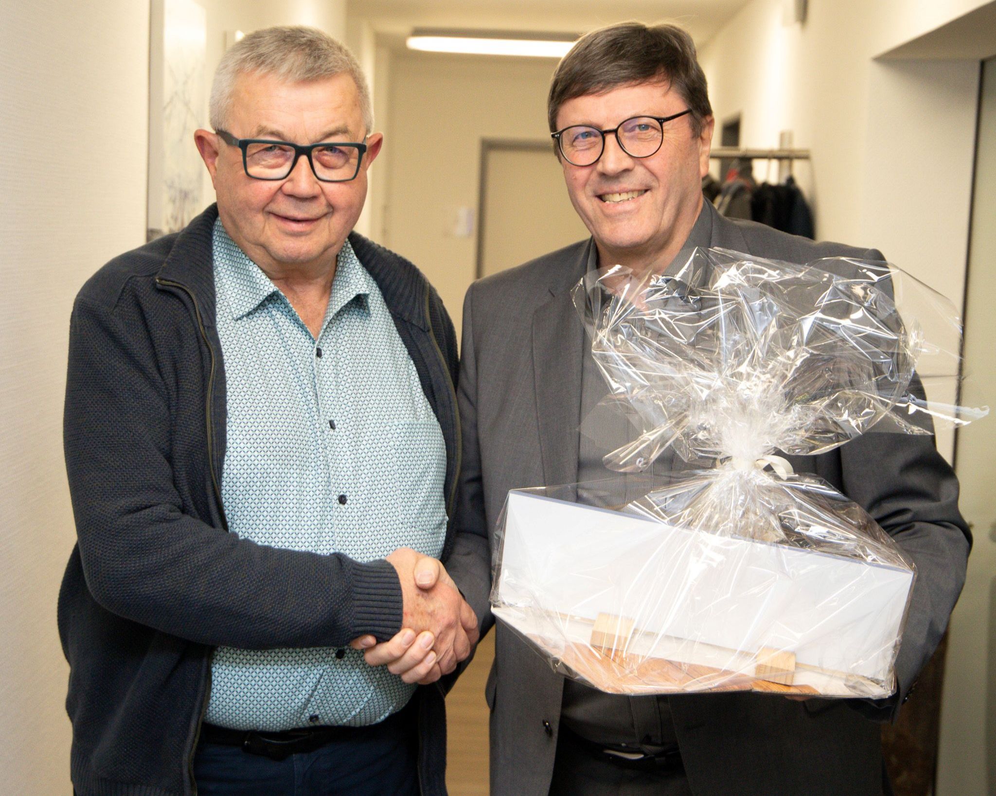 Bernward Wigger (rechts) überreicht Ludger Berges ein Geschenk, beide geben sich die Hand und lächeln in die Kamera. 