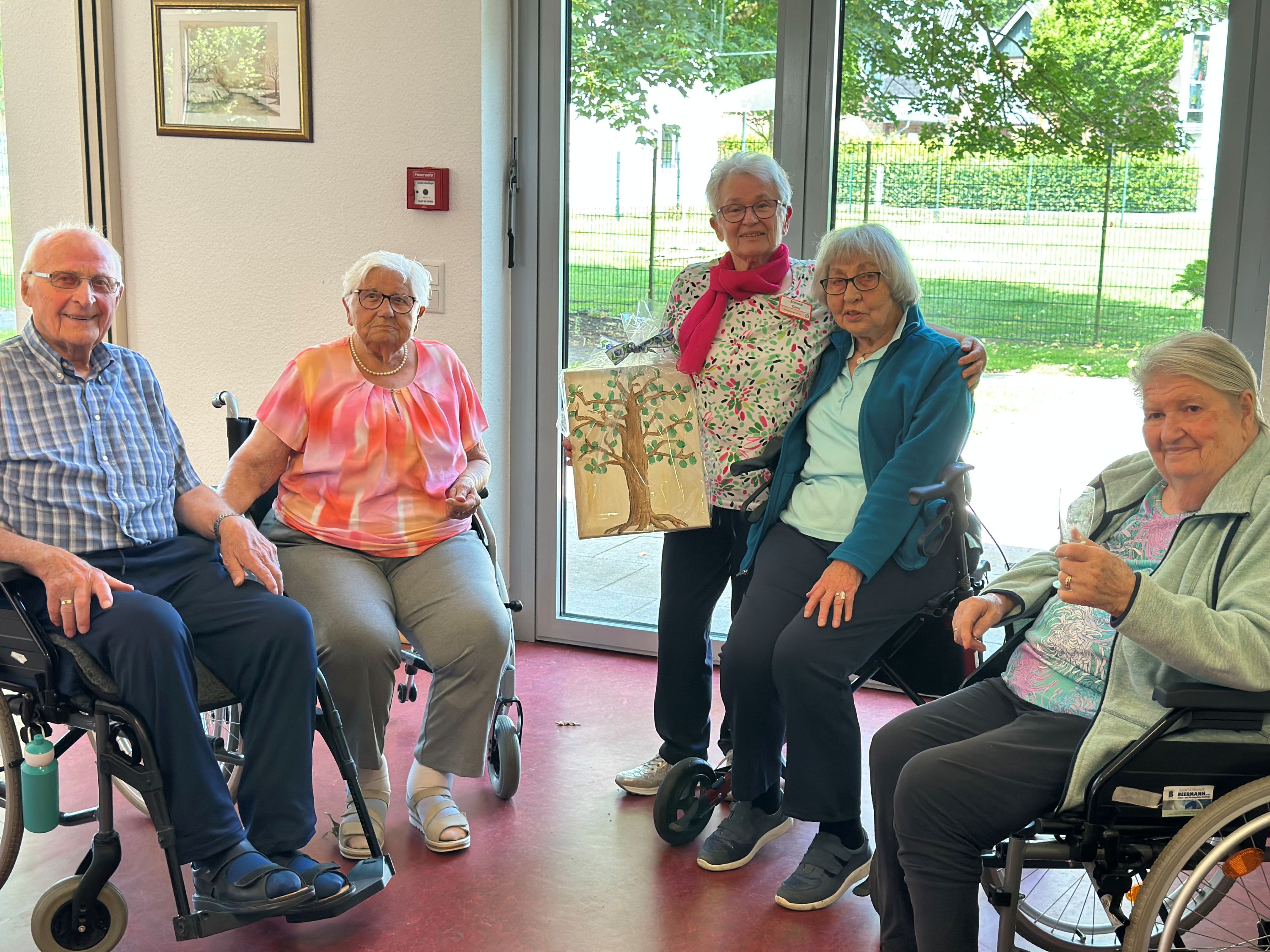 Drei Bewohnerinnen und ein Bewohner des Katharinen-Stifts (sitzend) freuen sich mit Doris Schmidt, der sie zum Abschied ein Bild geschenkt haben. 