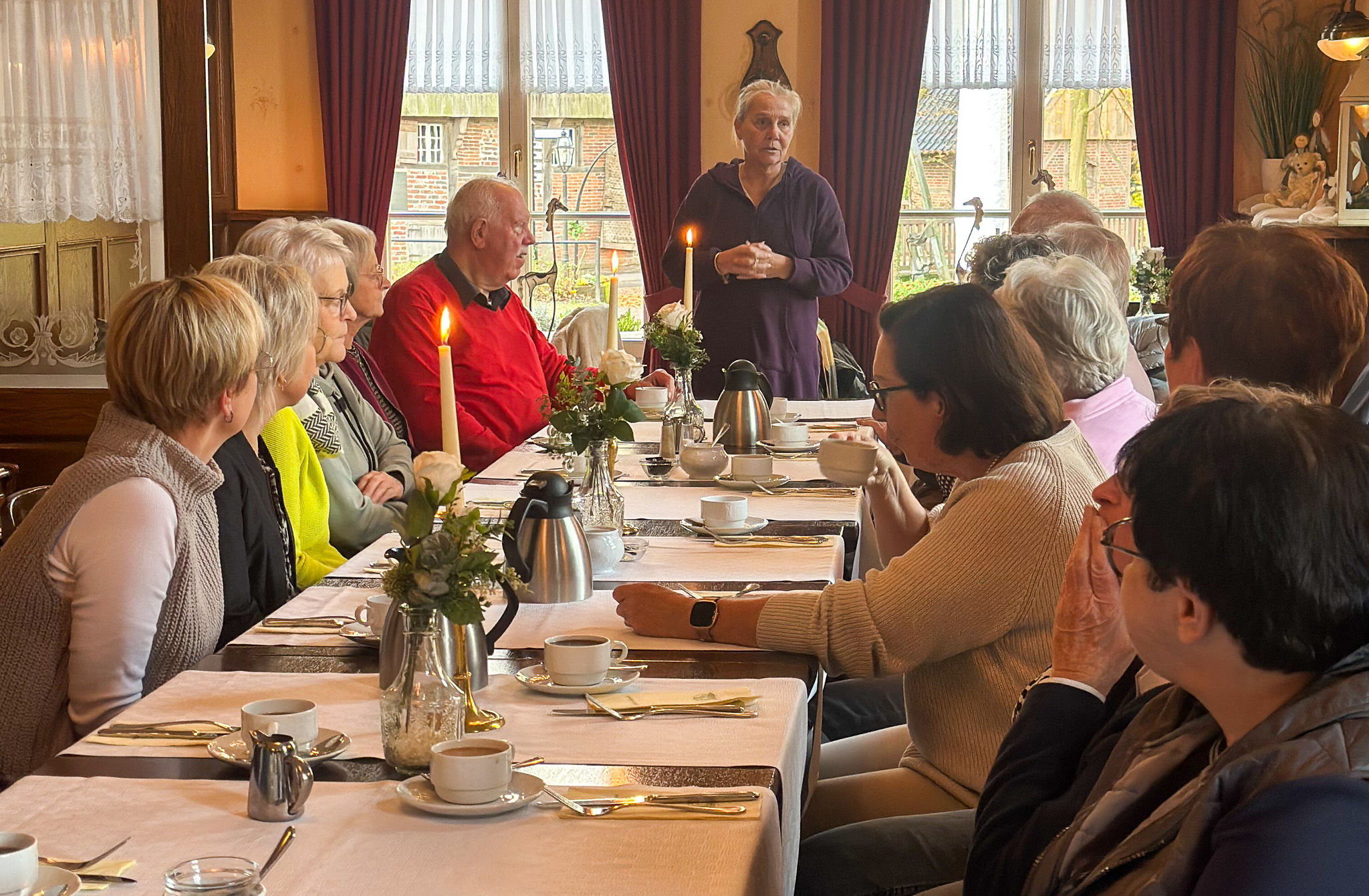Einrichtungsleiterin Marion van der Wals bedankte sich bei den Ehrenamtlern des Katharinenstifts. Die Ehrenämtler des Katharinenstfts sitzen am Esstisch, während Hausleiterin Marion van der Wals sie stehend begrüßt.