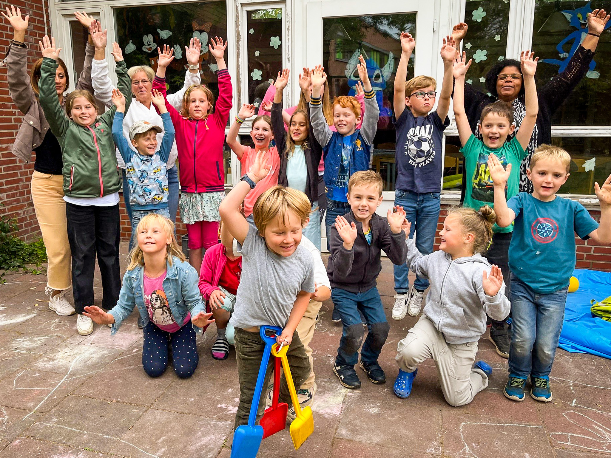 Kinder der Kinderferienbetreuung und Erzieher reißen für den Fotografen die Arme hoch und freuen sich.  