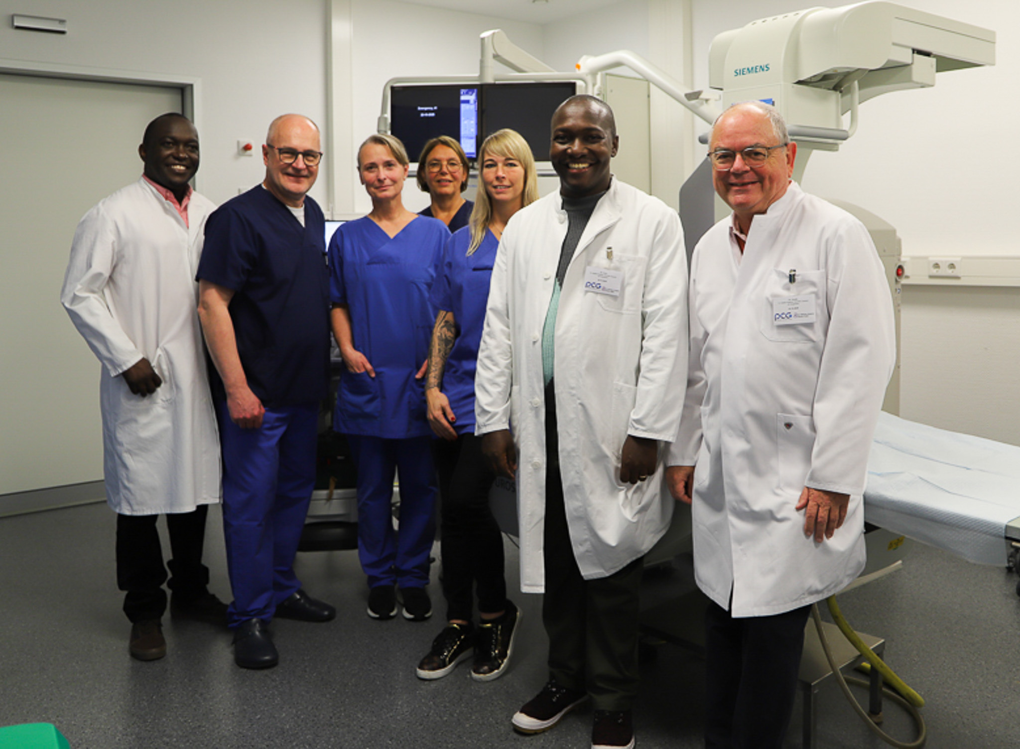 Von links: Dr. Titus Ndimbo, Dr. Jörg Zinke, Chefarzt der Urologie, Petra Blome, Endourologische OP- und Funktionseinheit, Ines Effing, Ltg. Patientenmanagement Ambulanz, Jacqueline von der Grinten, Ltg. Endourologische OP- und Funktionseinheit, Dr. Christopher Mfinanga und Dr. Ansgar Stüfe. Die beiden Ärzte aus Tansania neben Dr. Jörg Zinke und weiteren OP-Mitarbeiterinnen in einem Behandlungszimmer.