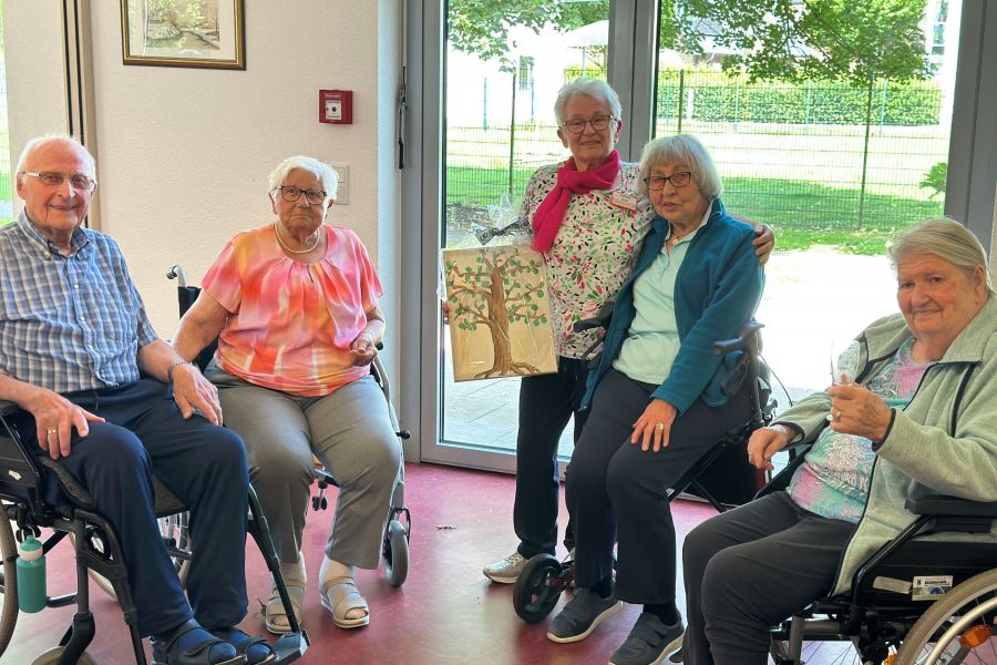 Drei Bewohnerinnen und ein Bewohner des Katharinen-Stifts (sitzend) freuen sich mit Doris Schmidt, der sie zum Abschied ein Bild geschenkt haben. 