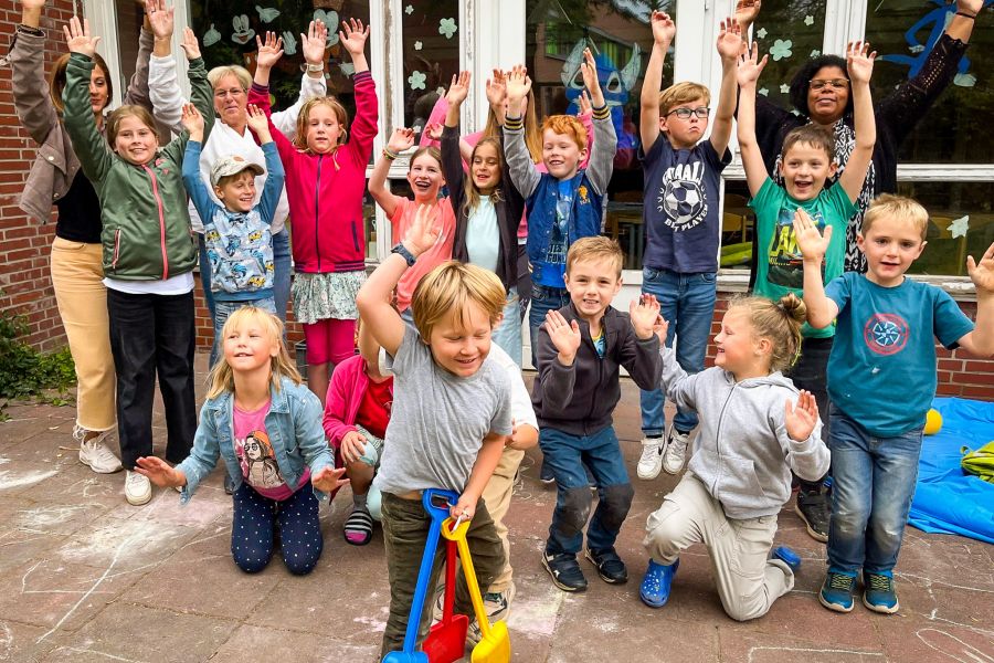 Kinder der Kinderferienbetreuung und Erzieher reißen für den Fotografen die Arme hoch und freuen sich.  