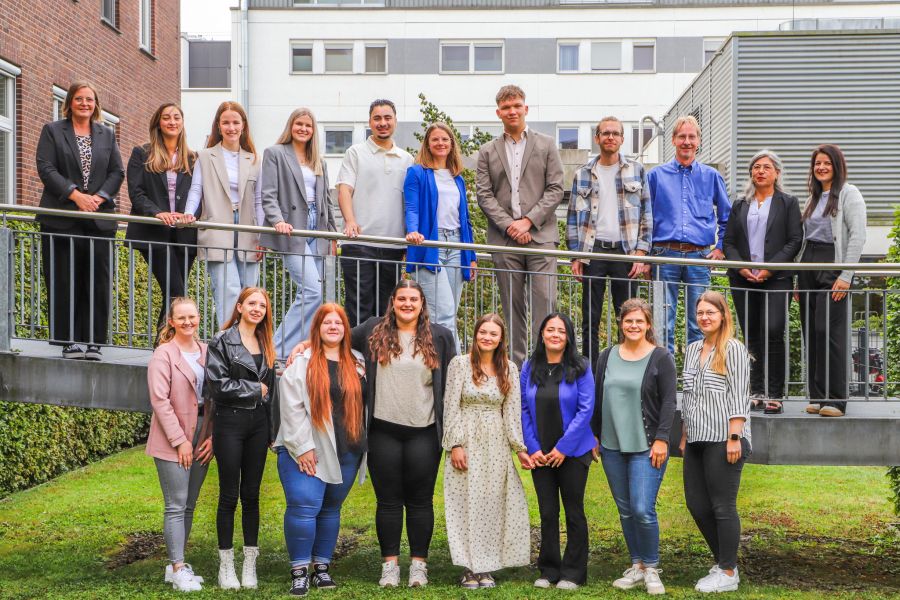 Die zwölf erfolgreichen Pflegeschülerinnen und Schüler stehen mit ihren Lehrerinnen und Lehrern vor dem Krankenhaus und lächeln in die Kamera. 