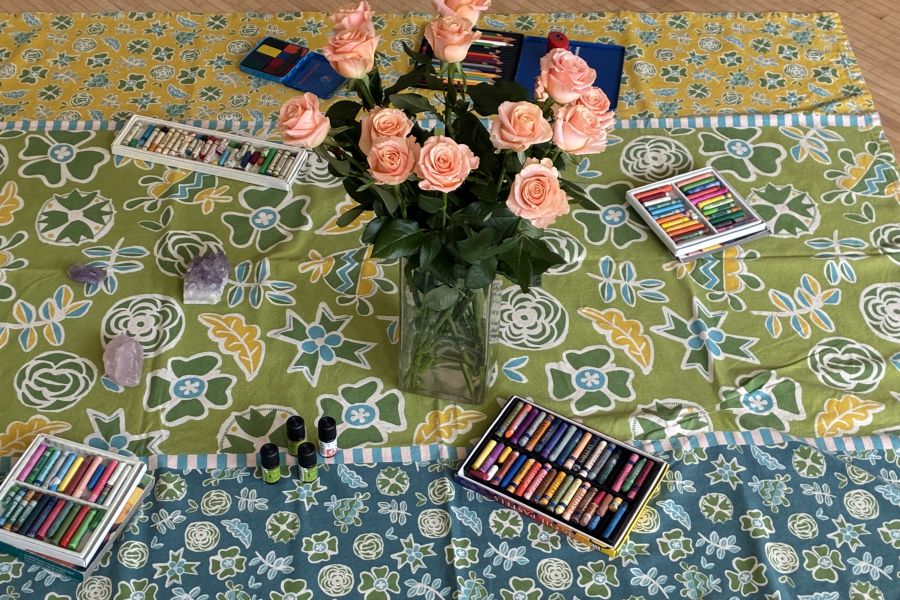 Das Stimmungsbild vom Seminar zeigt einen zartrosafarbenen Blumenstrauß in der Vase, Buntstifte auf einer Decke. 