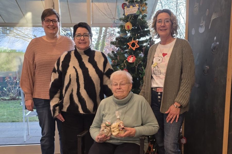 Marlies Kraan sitzt mit Plätzchentüte vor einem Weihnachtsbaum. Neben ihr Ursula Oude-Lansink, Verena Beyer und Nicole Köhler. 