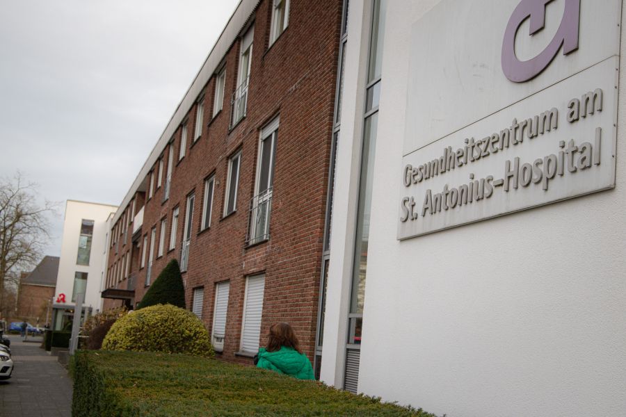 Blick auf das Gebäude des MVZ mit Schild Gesundheitszentrum im Vordergrund und einer Frau, die den Weg entlang läuft (von hinten). . 