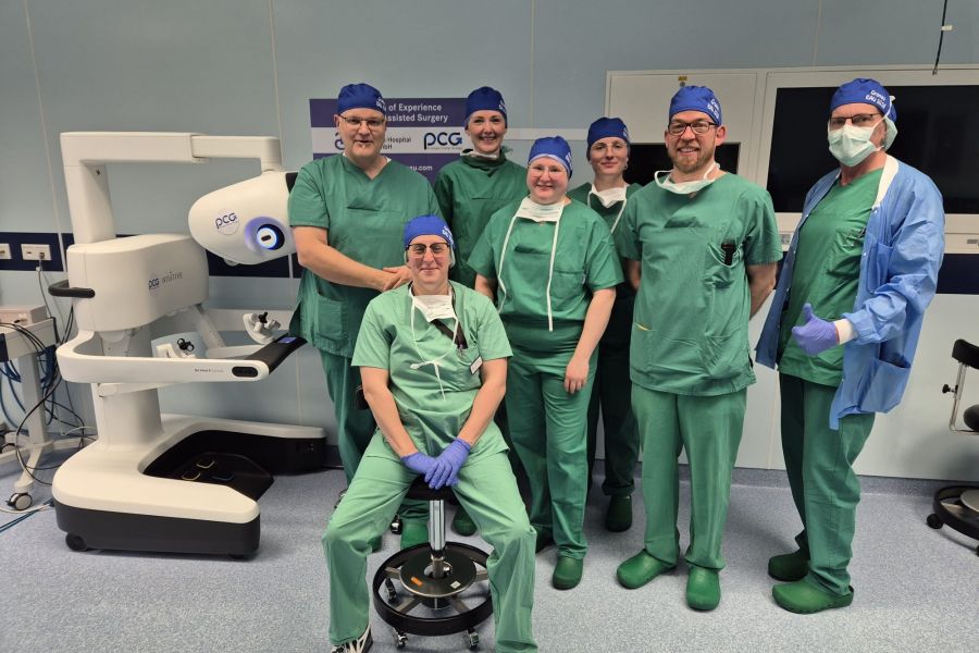 Das siebenköpfige Team stehend neben der Konsole des da Vinci 5 Operationssystems nach der Liveübertragung der radikalen Prostatektomie.  