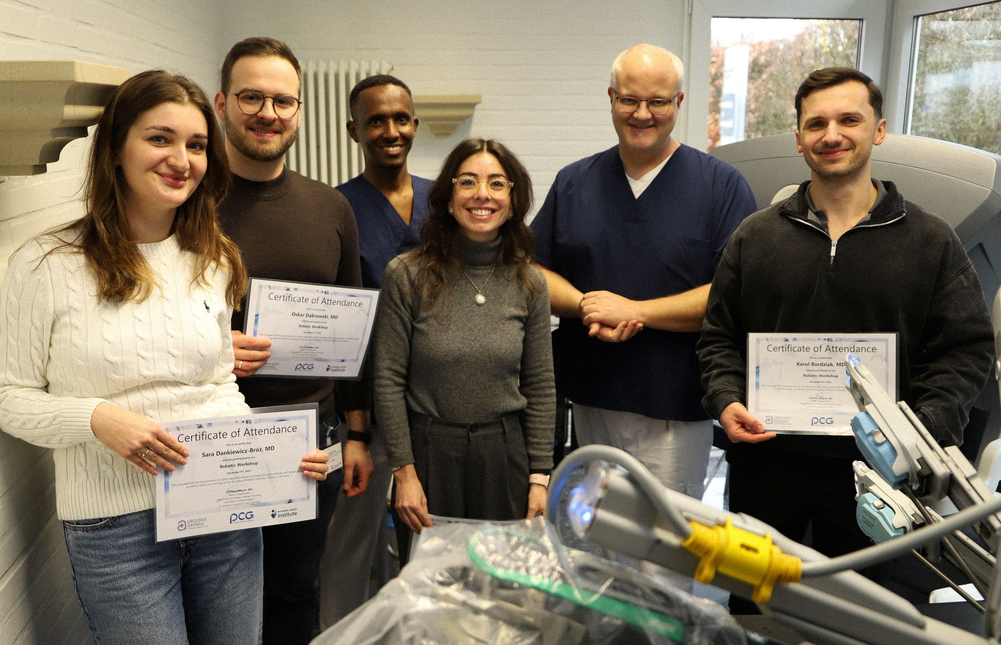 Sechs Ärzte stehen hinter den Armen des Trainingsroboters da Vinci im European Robotic Institute und lächeln in die Kamera. 