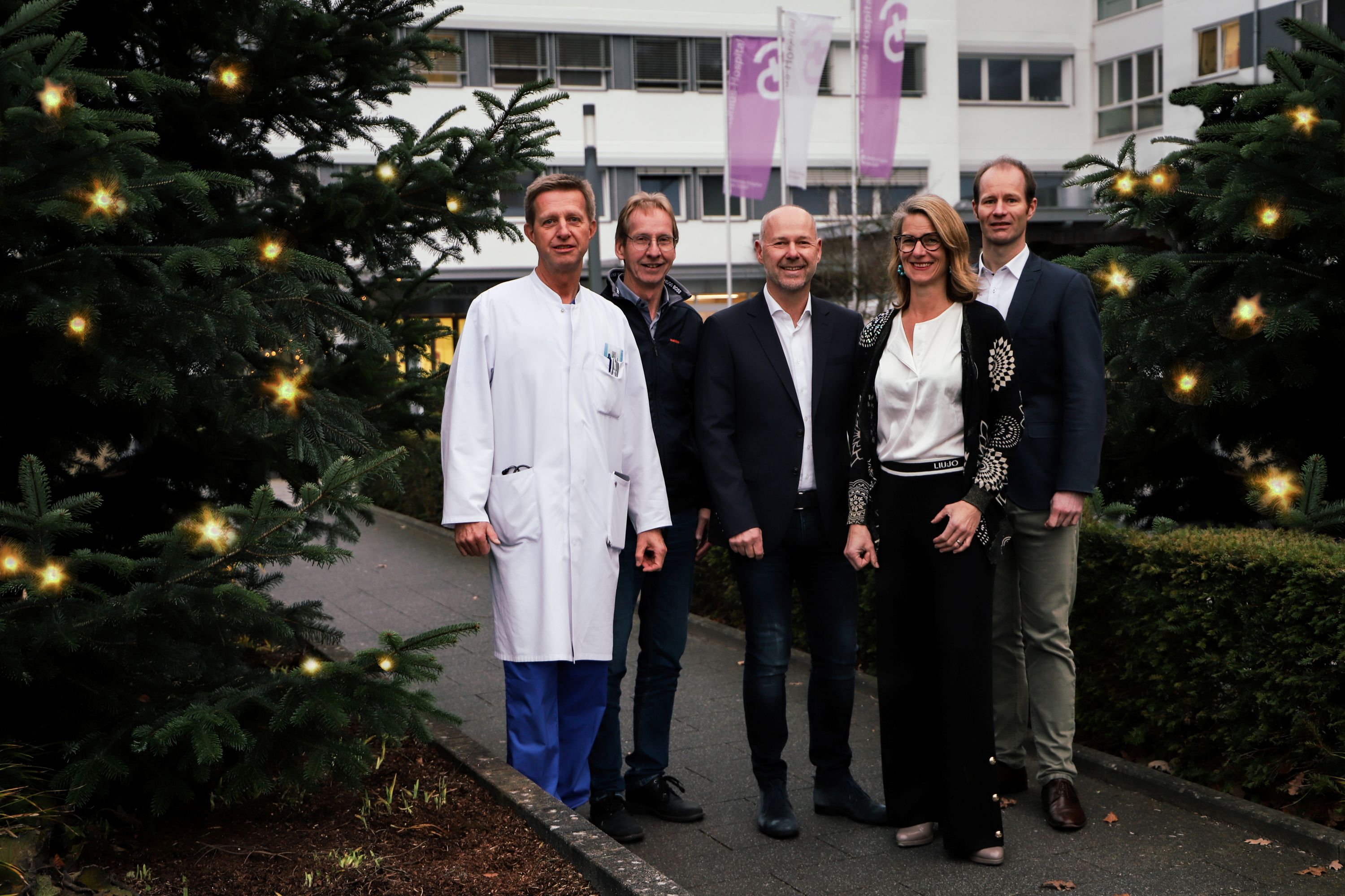 Die Betriebsleitung von links: Dr. Thomas Glosemeyer-Allhoff (Ärztlicher Direktor), Richard Mönning (Pflegedirektor), Christoph Bröcker (Geschäftsführer), Frauke Sonntag (Stv. Ärztliche Direktorin), Jens Breer (Geschäftsführer) vor dem Haupteingang des Krankenhauses mit Weihnachtsbaum zur linken und einen künstlich eingearbeiteten Weihnachtsbaum zur Rechten.  
