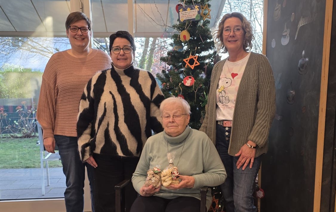 Marlies Kraan (sitzend) mit Dorotheenhof-Mitarbeiterin Ursula Oude-Lansink (rechts) sowie den beiden Mitarbeiterinnen des Grünen Warenhauses Verena Beyer (links und Nicole Köhler stellvertretend für das ganze Team. Marlies Kraan sitzt mit Plätzchentüte vor einem Weihnachtsbaum. Neben ihr Ursula Oude-Lansink, Verena Beyer und Nicole Köhler.