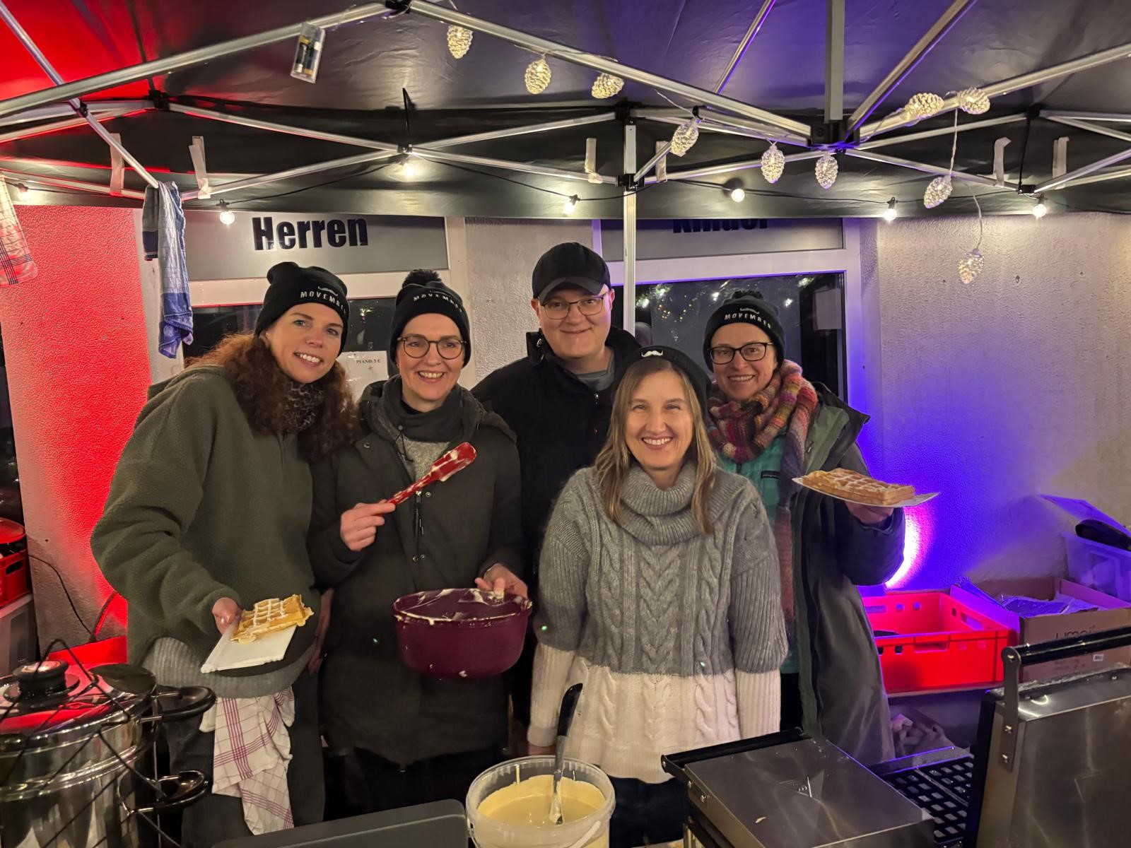 Der Weihnachtsmarktstand des Teams Bärte ohne Grenzen zog auch dieses Jahr wieder zahlreiche Besucher an. Ein Teil des Teams Bärte ohne Grenzen - Dr. Christian Wagner und vier Damen - stehen Tresen des Weihnachtsmarktstands in Bad Bentheim und verkaufen Waffeln und lächeln dabei in die Kamera. .