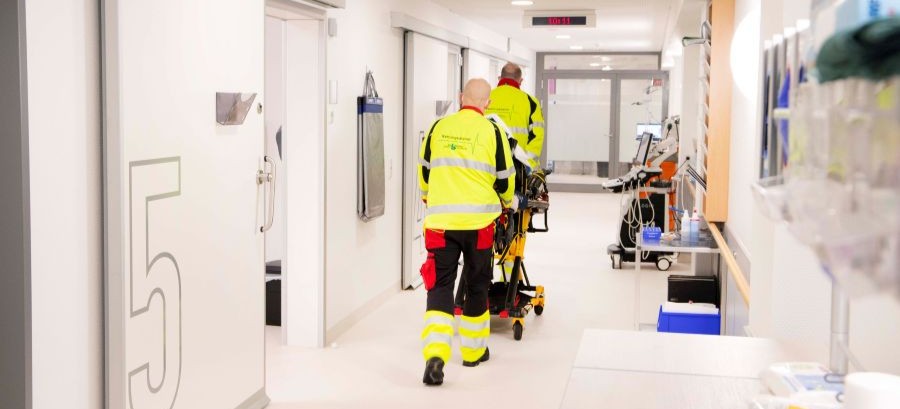 Rettungssanitäter schieben einen Notfallpatienten auf einer Liege durch einen Klinikflur in die Notaufnahme. 